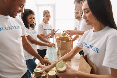 multiethnic group of volunteers putting food and drinks in paper bags for charity