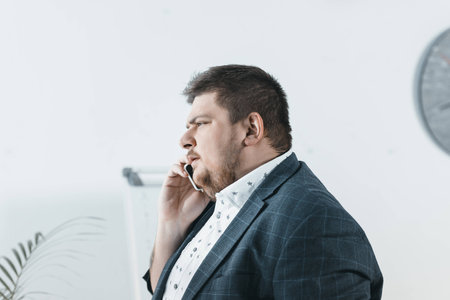 overweight businessman talking on smartphone in officeの写真素材
