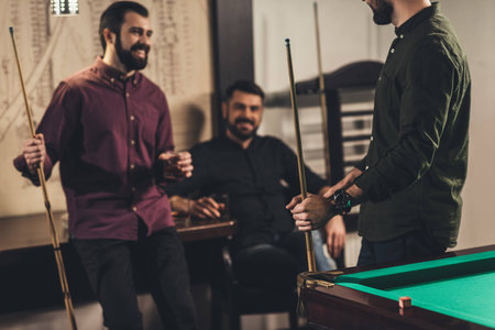 company of happy men with drinks and cues at billiard bar
