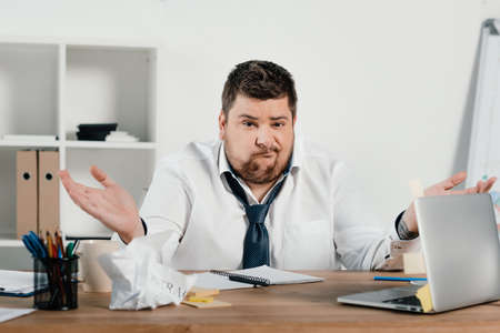 confused overweight businessman sitting at workspace with documents and laptop