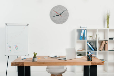 workplace with laptop and office supplies in office with white board and clockの写真素材