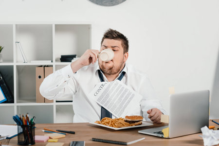 fat businessman eating fast food and drinking coffee in office