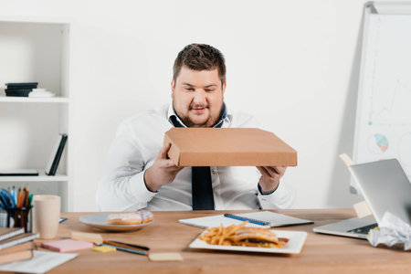 overweight businessman eating pizza at workplaceの写真素材
