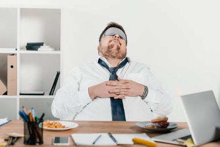 overweight businessman in sleeping mask relaxing at workplaceの写真素材