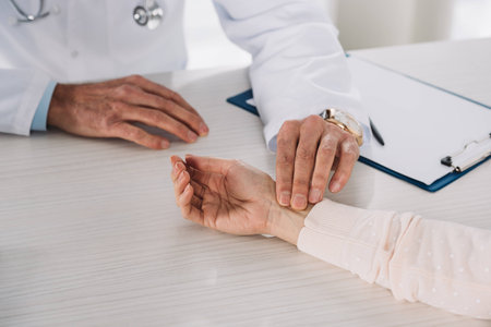 cropped image of doctor measuring female patient pulse