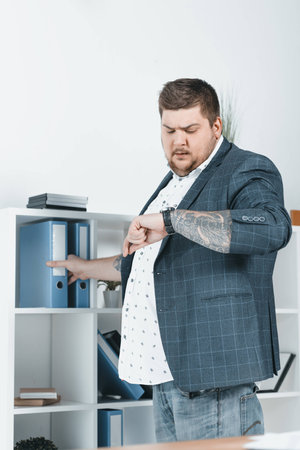 overweight businessman looking at watch while taking folders with documentsの写真素材