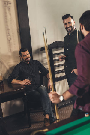 company of happy men with drinks and cues at billiard bar