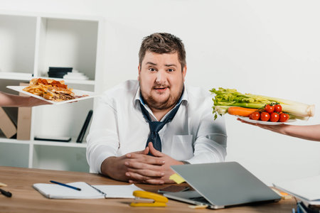overweight businessman choosing healthy or junk food at workplace in officeの写真素材