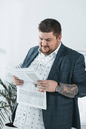 fat businessman in suit reading newspaper in officeの写真素材