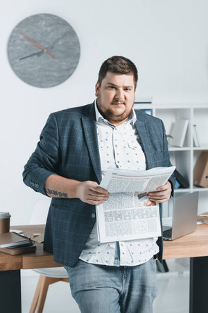 overweight businessman in suit reading newspaper at workplaceの写真素材
