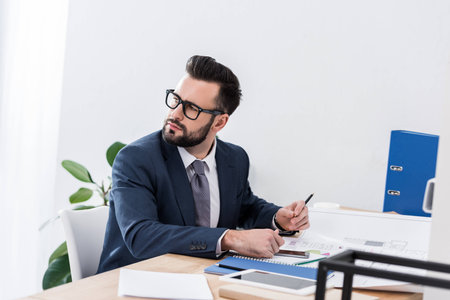 thoughtful businessman sitting at working table and looking awayの写真素材