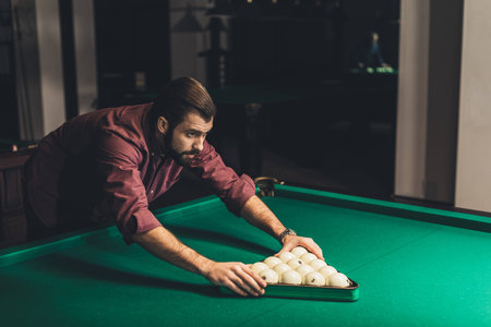 handsome man forming triangle of russian pool balls at bar