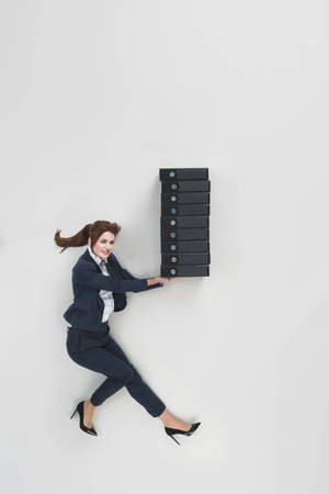 overhead view of smiling businesswoman holding pile of folders isolated on greyの写真素材