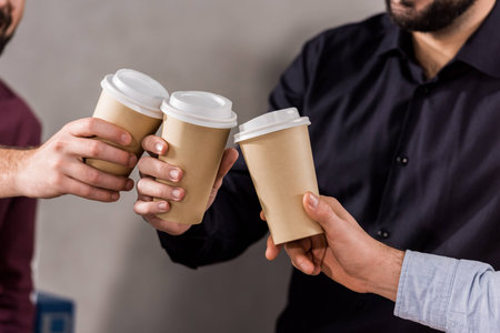 cropped image of businessmen clinking with disposable coffee cupsの写真素材