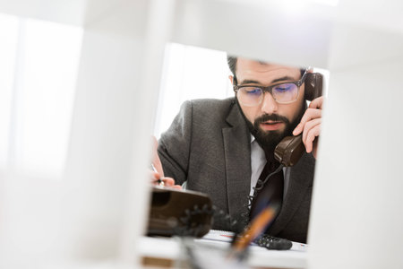 view through partition on businessman talking by stationary telephone in office