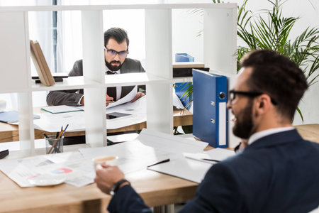 businessmen sitting at working tables with partition between themの写真素材