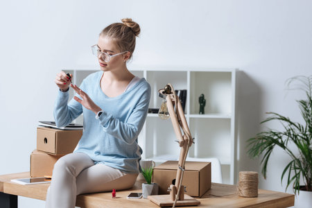 portrait of young woman applying nail polish while sitting on table at homeの写真素材