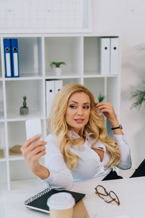 sexy blonde businesswoman taking selfie at working place with smartphoneの写真素材