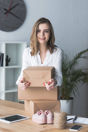 portrait of smiling self-employed businesswoman with parcels looking at camera at home officeの写真素材