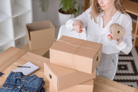 partial view of entrepreneur packing customers purchase in cardboard boxes at home officeの写真素材
