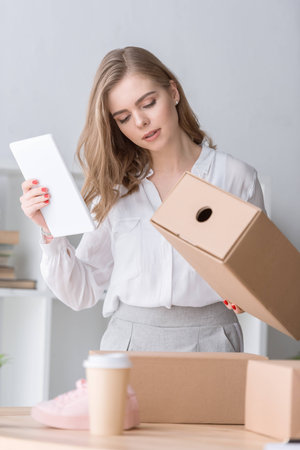 portrait of young businesswoman with cardboard box and tablet in handsの写真素材