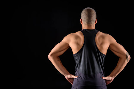 rear view of muscular african american sportsman standing isolated on blackの写真素材