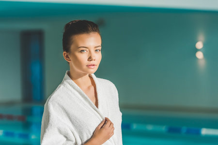 beautiful young woman in bathrobe in front of swimming pool at spaの写真素材