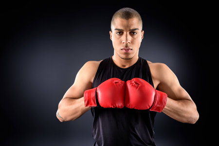 handsome african american sportsman in boxing gloves looking at camera on black