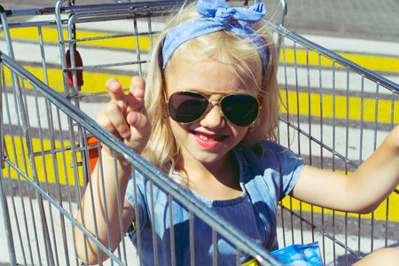 little stylish female child in sunglasses having fun in shopping cartの写真素材