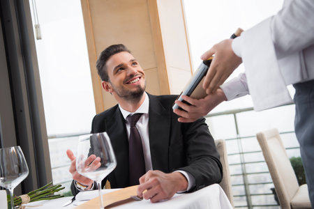 partial view of smiling man looking at waiter with bottle of wine in restaurantの写真素材
