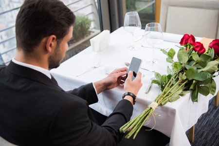 side view of man in suit using smartphone while waiting for girlfriend in restaurantの写真素材