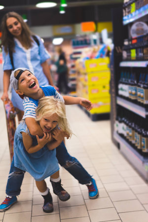 happy siblings having fun in supermarket, mother standing behindの写真素材