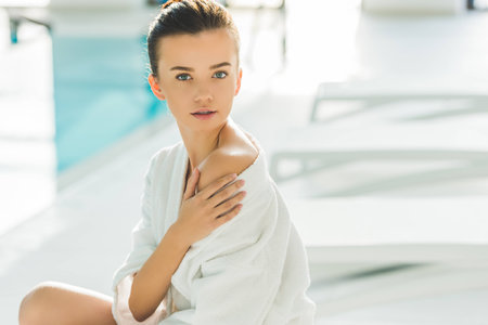 beautiful young woman in bathrobe with naked shoulder touching her skin at spa