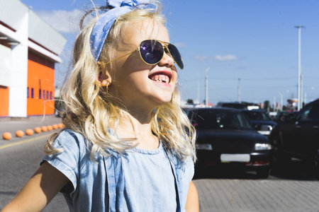 stylish cheerful adorable kid in sunglasses standing on parking with carsの写真素材
