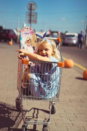 little adorable smiling kid sitting in shopping cart with skateboardの写真素材