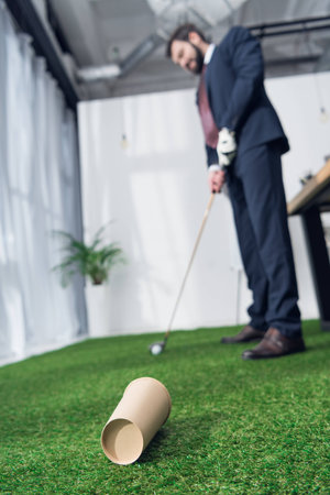 selective focus of young businessman playing golf in officeの写真素材