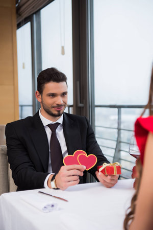 partial view of young man presenting gift to girlfriend on romantic date in restaurantの写真素材