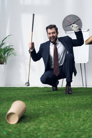 excited young businessman playing golf in officeの写真素材