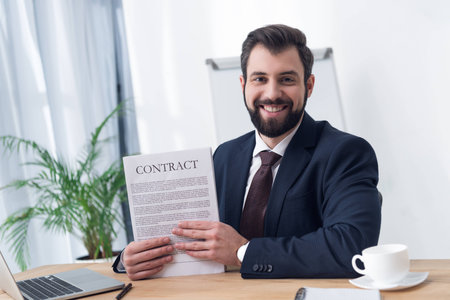 portrait of smiling businessman with contract at workplace in officeの写真素材