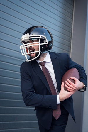 young angry businessman in suit and rugby helmet with ball in hands on streetの写真素材