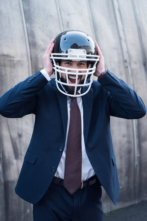 portrait of excited businessman in suit and rugby helmet on streetの写真素材