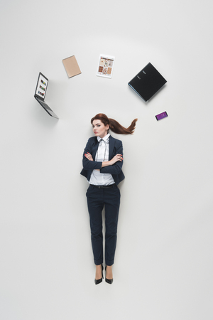 overhead view of businesswoman with various office supplies above head isolated on greyのeditorial素材