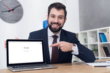 portrait of smiling businessman pointing at laptop at workplace in officeのeditorial素材