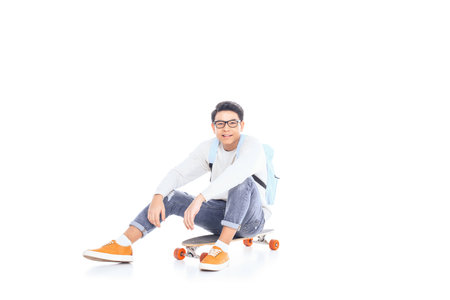 asian teenager with backpack sitting on skateboard isolated on whiteの写真素材