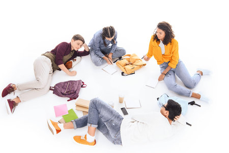 high angle view of interracial students with notebooks and backpacks resting isolated on whiteの写真素材