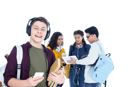 handsome teen student in headphones and with smartphone isolated on white with his friends chatting on backgroundの写真素材