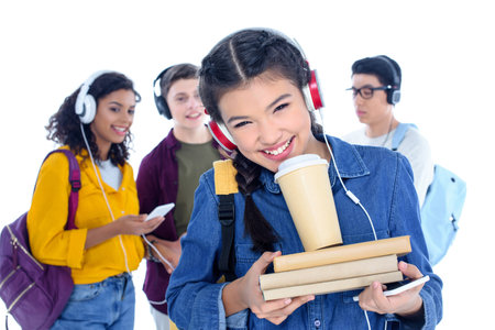 teen student girl in headphones with coffee to go isolated on white with her friends chatting on backgroundの写真素材
