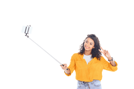 portrait of smiling african american teenager taking selfie on smartphone isolated on whiteの写真素材