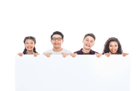 portrait of smiling multiracial teenagers holding blank banner together isolated on white