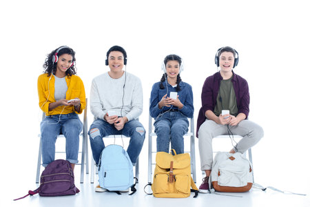group of teen students in headphones sitting on chairs isolated on whiteの写真素材